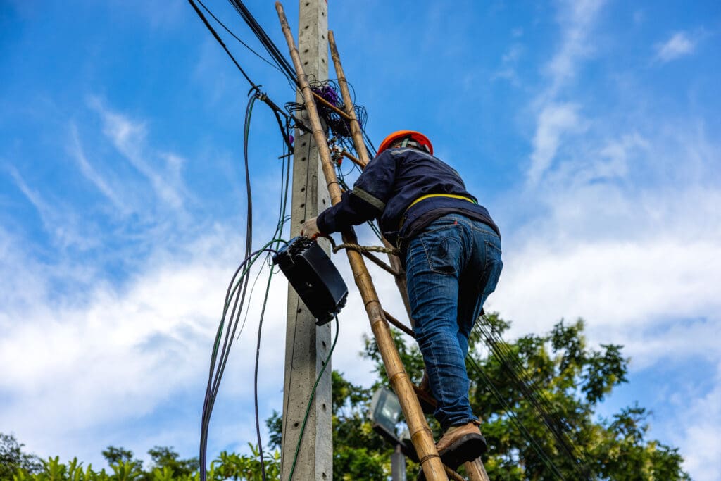 A telecoms worker is shown working from a utility pole ladder